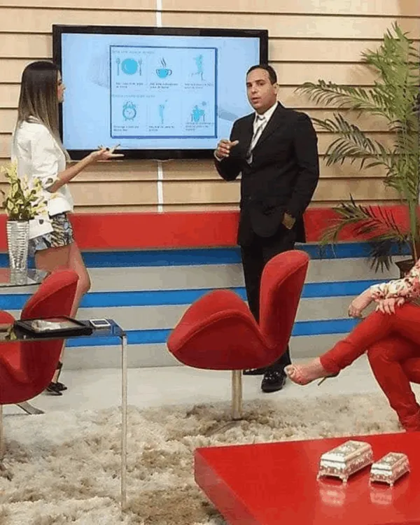 Juliano Lopes explica a hipnose diante de um telão em programa de TV